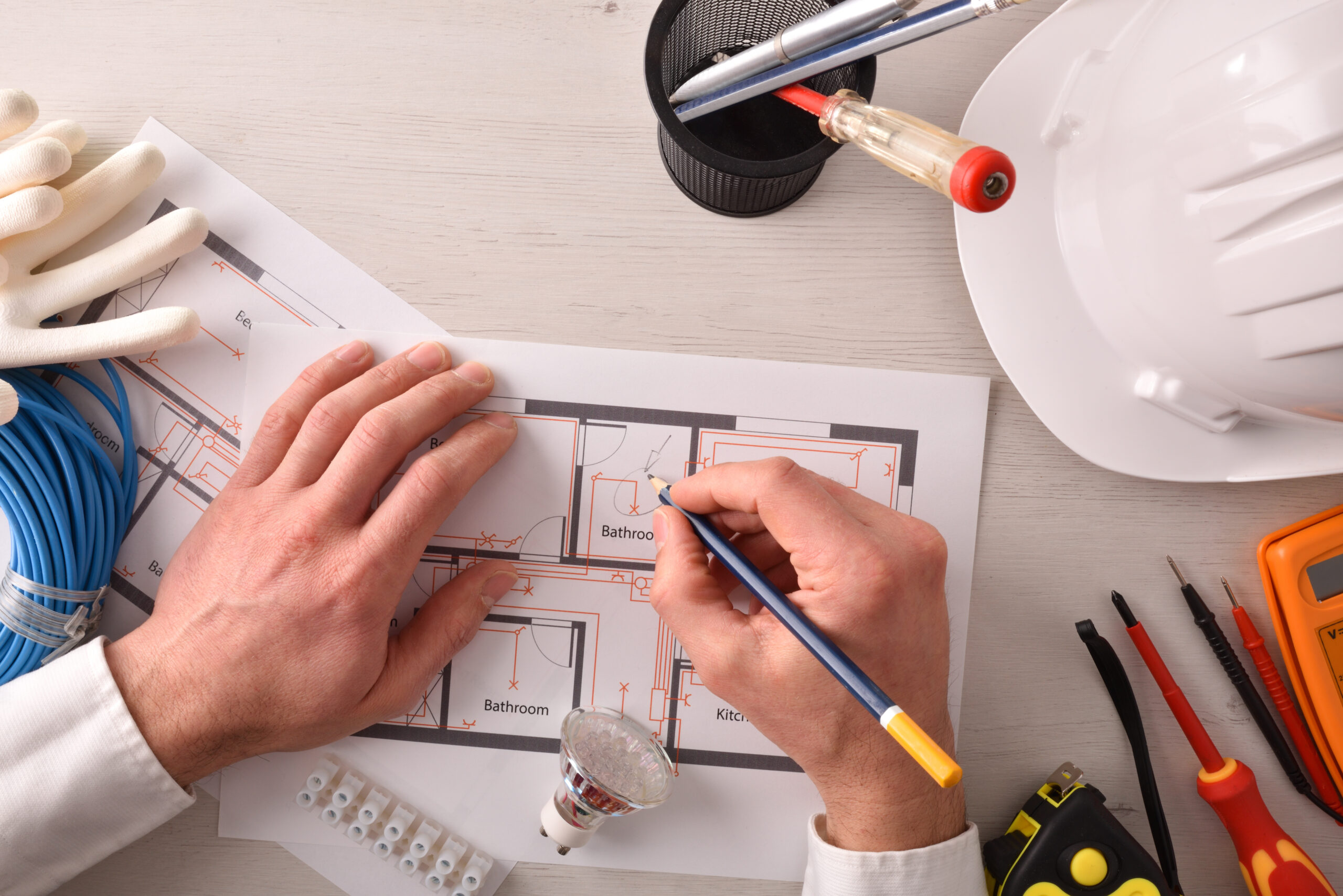 Technical engineer in electricity writing in an electrical diagram of housing installation on the desk with tools around. Horizontal composition. Top view.